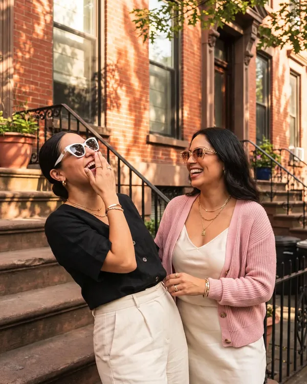 Two friends laughing on a Harlem stoop wearing the Ivory Cat-Eye and Champagne Chain sunglasses